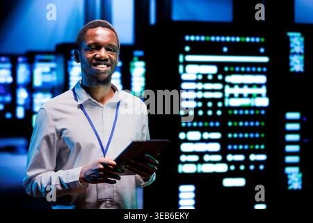 Portrait of smiling overseerer running data center devices diagnostic tests to determine and debug software problems. Happy serviceman using tablet to analyze critical systems, checking for crashes Stock Photo