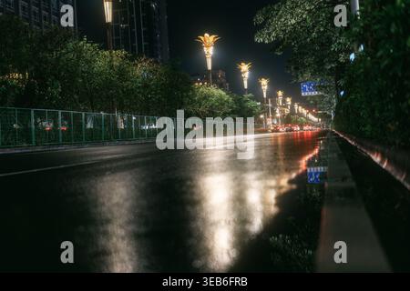 Nighttime city street with wet asphalt reflecting golden lampposts and car lights, urban nightlife Stock Photo