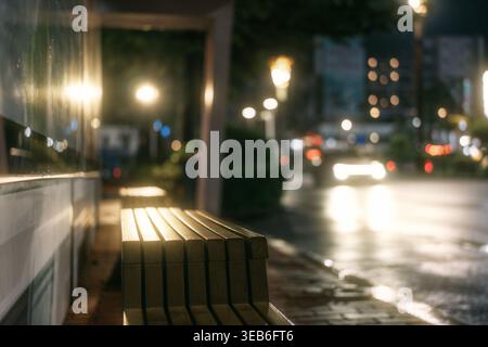 Rainy Night Street Scene with Wooden Bench and Bokeh City Lights Stock Photo