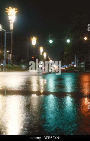 Rainy Night Street with Wet Reflections, Blurred Motorbike Traffic and Illuminated Lampposts Stock Photo