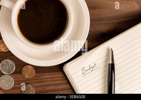 Open Notebook with “Budget” Written on Page, Coins and Coffee – Personal Finance Concept Stock Photo
