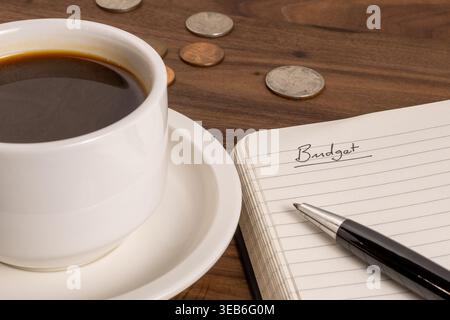 Open Notebook with “Budget” Written on Page, Coins and Coffee – Personal Finance Concept Stock Photo