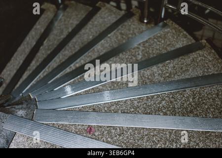 Close-up of metallic stair treads with ribbed texture arranged radially on speckled stone floor, Stock Photo