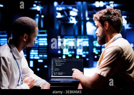 IT developers coworkers writing script code in server room on laptop terminal. Teamworking programmers doing maintenance work in technologically advanced data center updating racks software Stock Photo