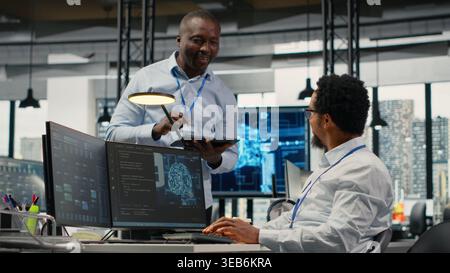 Smiling programmers working in AI startup train predictive models for language processing tasks. Cheerful IT professionals use machine learning technical expertise for complex tasks, camera B Stock Photo