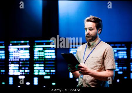 Admin walking in data center supporting AI through powerful computing operations, hosting specialized storage servers. Engineer ensuring high tech facility internal hardware functions properly Stock Photo