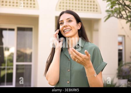 Smiling woman standing outdoors and talking on smartphone Stock Photo