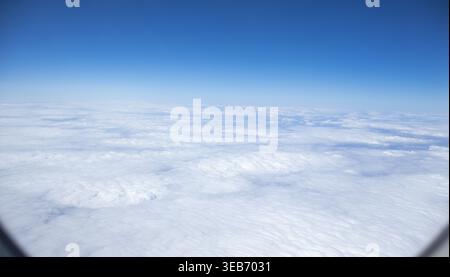 Vast expanse of white fluffy clouds viewed from an airplane window under a clear blue sky Stock Photo