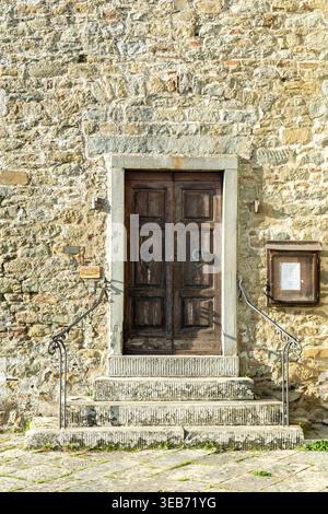 View of an ancient wooden double door with iron knockers set in a rustic stone wall with steps and handrails in the historic village of Loro Ciuffenna Stock Photo