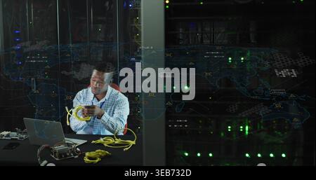 Coiling IT technician in light blue shirt at data center, with yellow Ethernet cables and laptop Stock Photo
