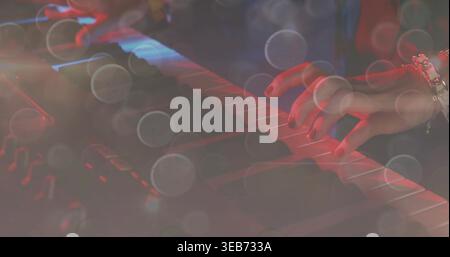 Playing musician's right hand pressing keyboard keys on stage, with dark sleeve, bracelet and bokeh Stock Photo