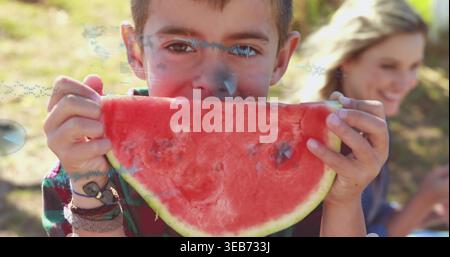 Biting child wearing plaid flannel shirt holding watermelon slice at park, with bracelets and watch Stock Photo