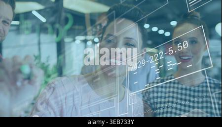 Collaborating team in business writing on glass board at open office, showing UI numbers and marker Stock Photo