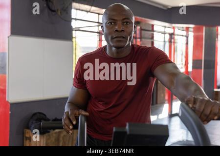 African American man working out on cardio machine gripping handlebars in gym near plyometric box Stock Photo