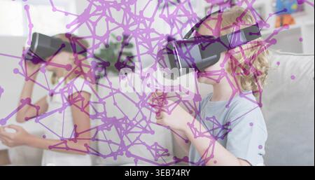 Playing two girls with controllers at home, wearing VR headsets and pale shirts, purple net overlay Stock Photo