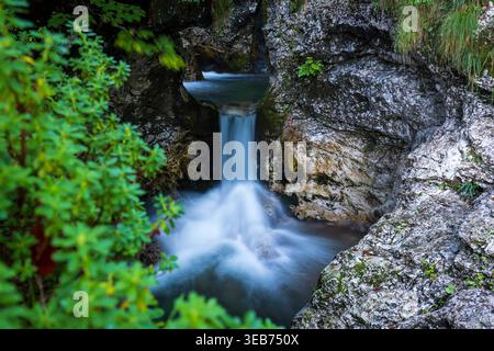10 September 2022: View of a small waterfall cascading between mossy rocks and lush green foliage in a secluded forest ravine. Stock Photo
