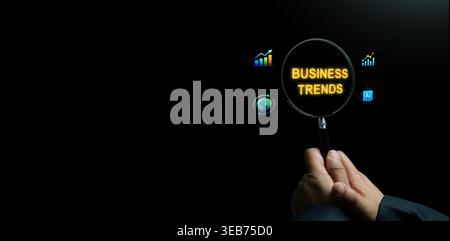 Business trends concept with a hand holding a magnifying glass over golden text, highlighting global economic growth, AI technology, and data analytic Stock Photo