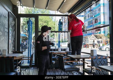 Batumi, georgia 21 april 2026: restaurant staff in batumi cleaning windows and tables inside a bright cafe, preparing for daytime service and welcomin Stock Photo