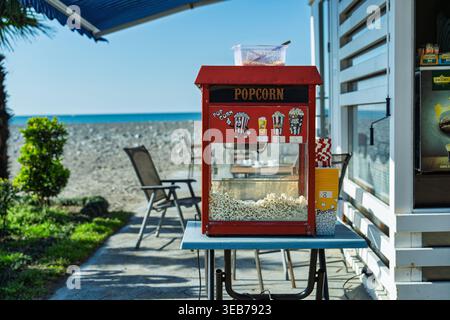 Batumi, georgia 21 april 2026: red vintage popcorn machine at a seaside snack counter, popping fresh popcorn on a sunny summer day by the black sea in Stock Photo