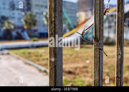 Batumi, georgia 21 april 2026: barbed wire coiled around rusty metal fence posts forming a sharp urban barrier in batumi, georgia, with blurred buildi Stock Photo