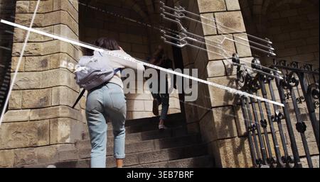 Walking two teen girls ascending stone steps at entrance, carrying striped and brown backpacks Stock Photo