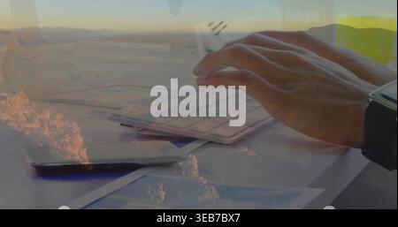 Typing right hand on slim keyboard at home desk, reflecting desert overlay, dark smartwatch, phone Stock Photo