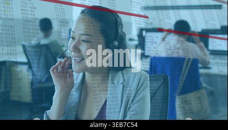 Smiling Asian service agent wearing gray blazer adjusting headset at call center with data overlay Stock Photo