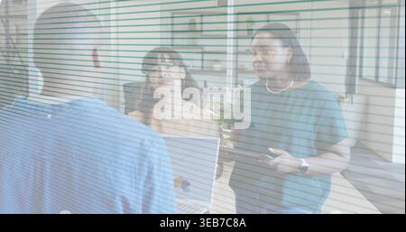 Showing, three staff in blue shirt, green top talking at reception counter, open laptop tablet Stock Photo