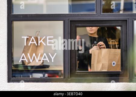 Batumi, georgia 21 april 2026: woman employee giving take away food in paper bags through a window. Restaurant offering delivery service for customers Stock Photo