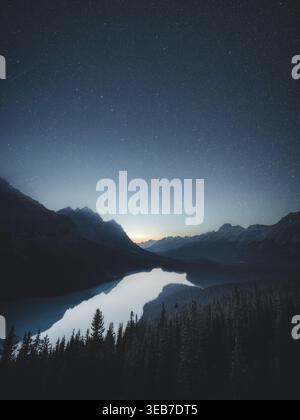 View of Peyto Lake surrounded by dark mountain peaks and evergreen forests under a starry night sky Canada. Stock Photo