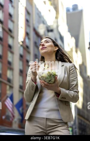 Young businesswoman standing outdoors in new york city, taking a healthy lunch break with a fresh salad, reflecting urban professional lifestyle and w Stock Photo
