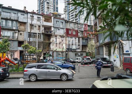 Batumi, georgia 21 april 2026: batumi, georgia, featuring a weathered and colorful residential building facade, modern apartment towers, cars, and peo Stock Photo
