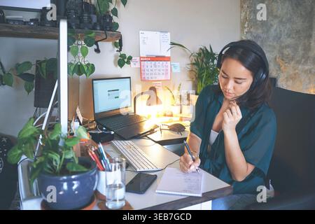 Notebook, woman or tech with headset in home office for admin planner, scheduling or remote work. Laptop screen, virtual assistant or writing notes at Stock Photo