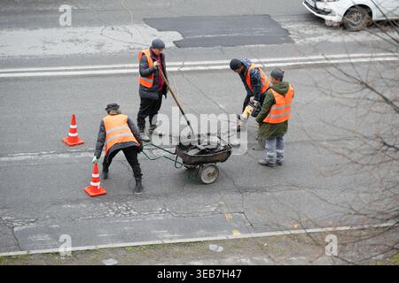 VLADIKAVKAZ, RUSSIA - APRIL  26 , 2024:   Group of road workers in orange vests repairing asphalt on a city street.  Road construction crew using a ja Stock Photo
