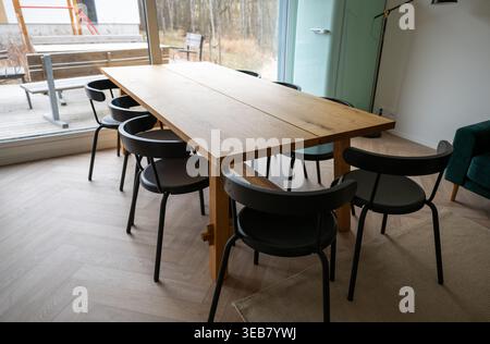 Modern wooden dining table with black chairs in minimalist kitchen interior near window Stock Photo