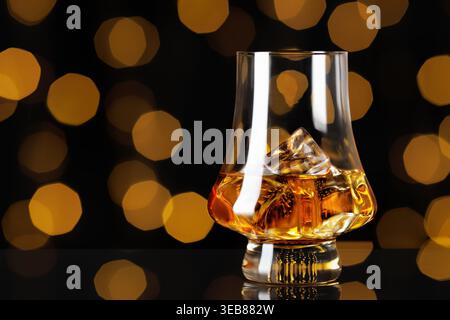 Amber whiskey with melting ice cubes in a clear glass, creating rich golden hue against warm, blurred bokeh backdrop Stock Photo