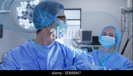 Standing male surgeon crossing arms and female nurse wearing blue gowns in OR, with overhead lights Stock Photo