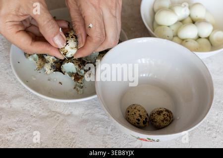 Woman peeling boiled quail eggs in kitchen, closeup Stock Photo