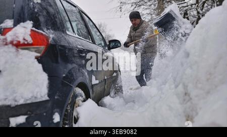 Man shoveling deep snow from around a car during a harsh winter blizzard Stock Photo