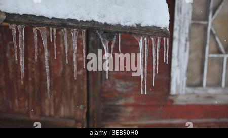 Icicles hanging from a weathered roof ledge over red barn wall Stock Photo