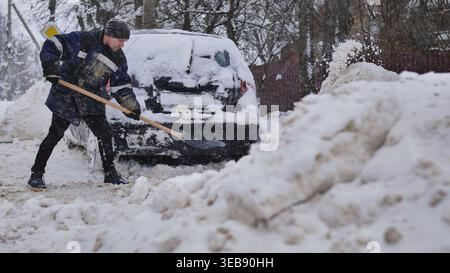 Man shoveling deep snow from car during harsh winter blizzard aftermath Stock Photo