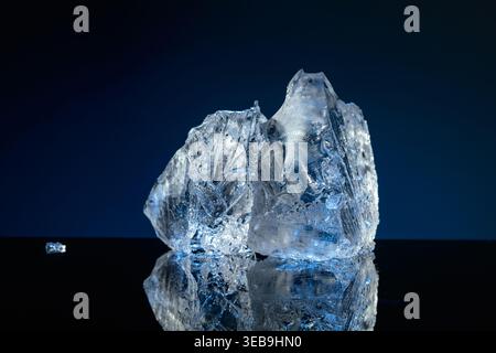 Broken ice with blue backlight on a black reflective background. Copy space. Stock Photo