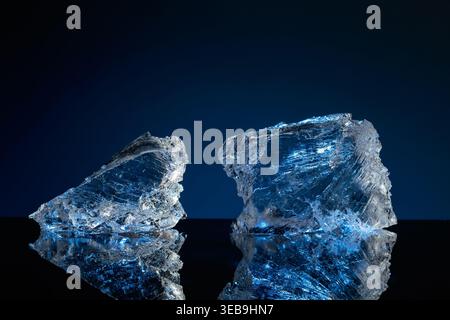 Broken ice with blue backlight on a black reflective background. Copy space. Stock Photo