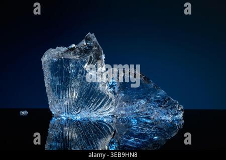 Broken ice with blue backlight on a black reflective background. Copy space. Stock Photo