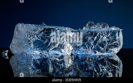 Broken ice with blue backlight on a black reflective background. Copy space. Stock Photo