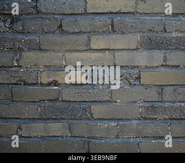 Reclaimed brick wall painted black with uneven chipped bricks, rough and smooth textures, worn paint revealing mortar and red brick, horizontal layout Stock Photo