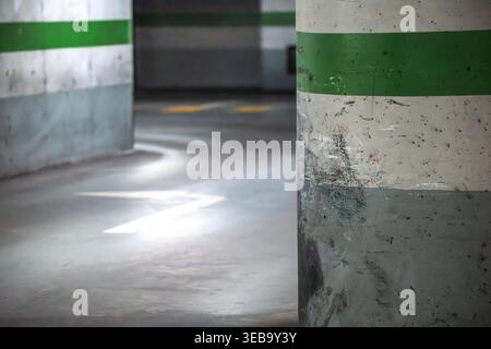 View of a scratched concrete pillar with a green stripe in an empty underground parking garage with painted arrows on the floor. Stock Photo
