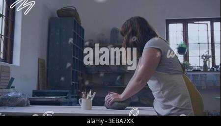 Shaping female potter wearing apron pressing damp lump of clay at studio worktable, with tools Stock Photo