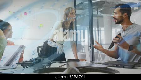 Leading woman in white blouse leaning on conference table, directing team with drone and tablet Stock Photo