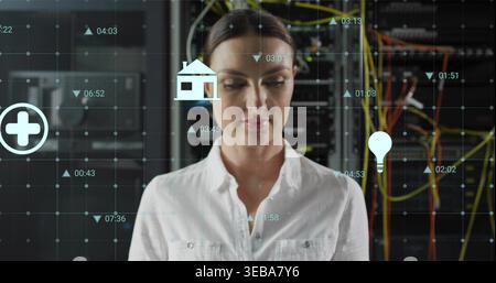 Standing female tech wearing white shirt watching server racks or switches with HUD icons and cables Stock Photo